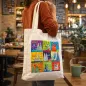 Preview: Köln Stofftasche mit Dom-Motiv über der Schulter getragen in gemütlichem Café, moderne Szene mit Holztischen und Tasse