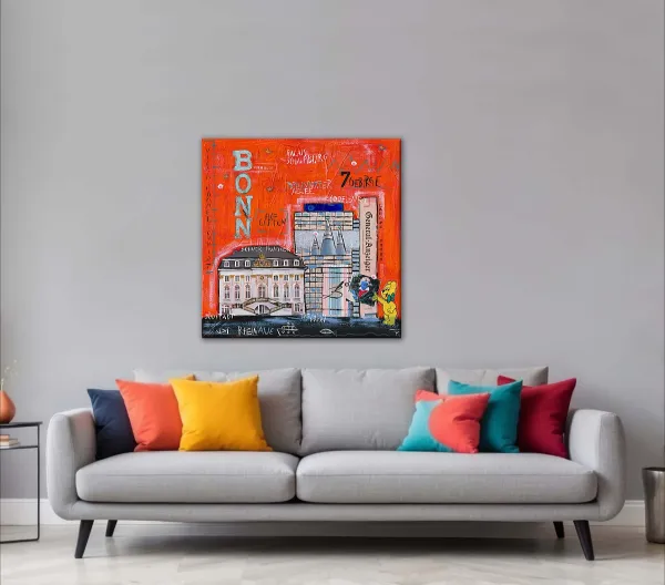 Wandbild Bonn-City in Orange über grauem Sofa mit bunten Kissen vor heller Wand.